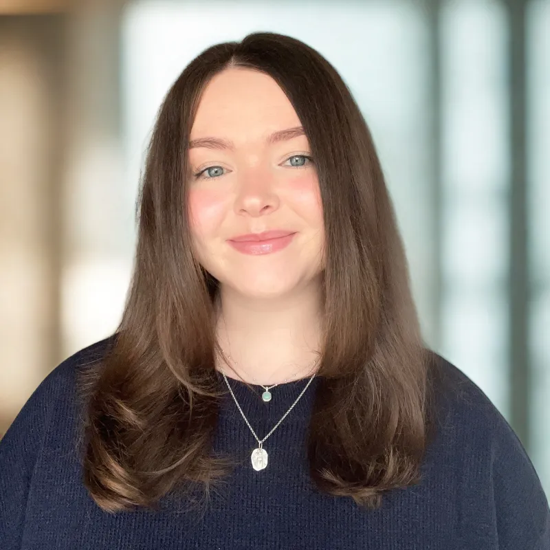 An image of a woman with shoulder length straight hair wearing a black blouse smiling and a blurred out background