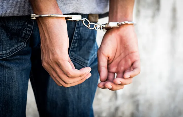 Close up hands tied up handcuffs in behind his body. Arrested man handcuffed hands at the back.