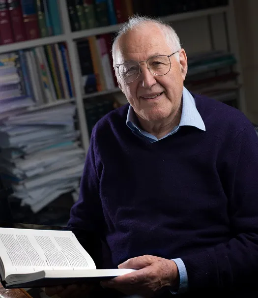 Professor Sir Roy Goode CBE KC FBA smiling, holding a book.