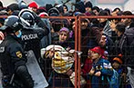 Refugees behind a fence with Croatian police standing guard