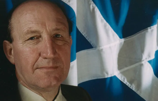 Neil MacCormick with the Scottish flag behind him.