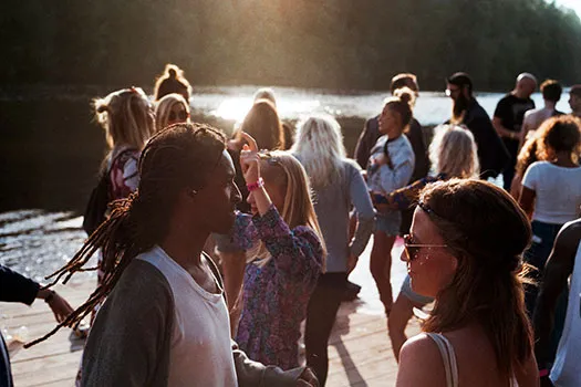 A party of people gathered by a river at sunset
