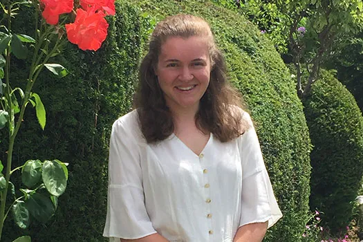 Lauren Holmes standing in front of a hedge with a pink flower to the left of her
