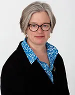 Julia Hornle wearing glasses, a black jumper and blue and white polka dot shirt.
