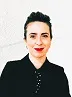 Clara Barbiani in black suit against white background, smiling