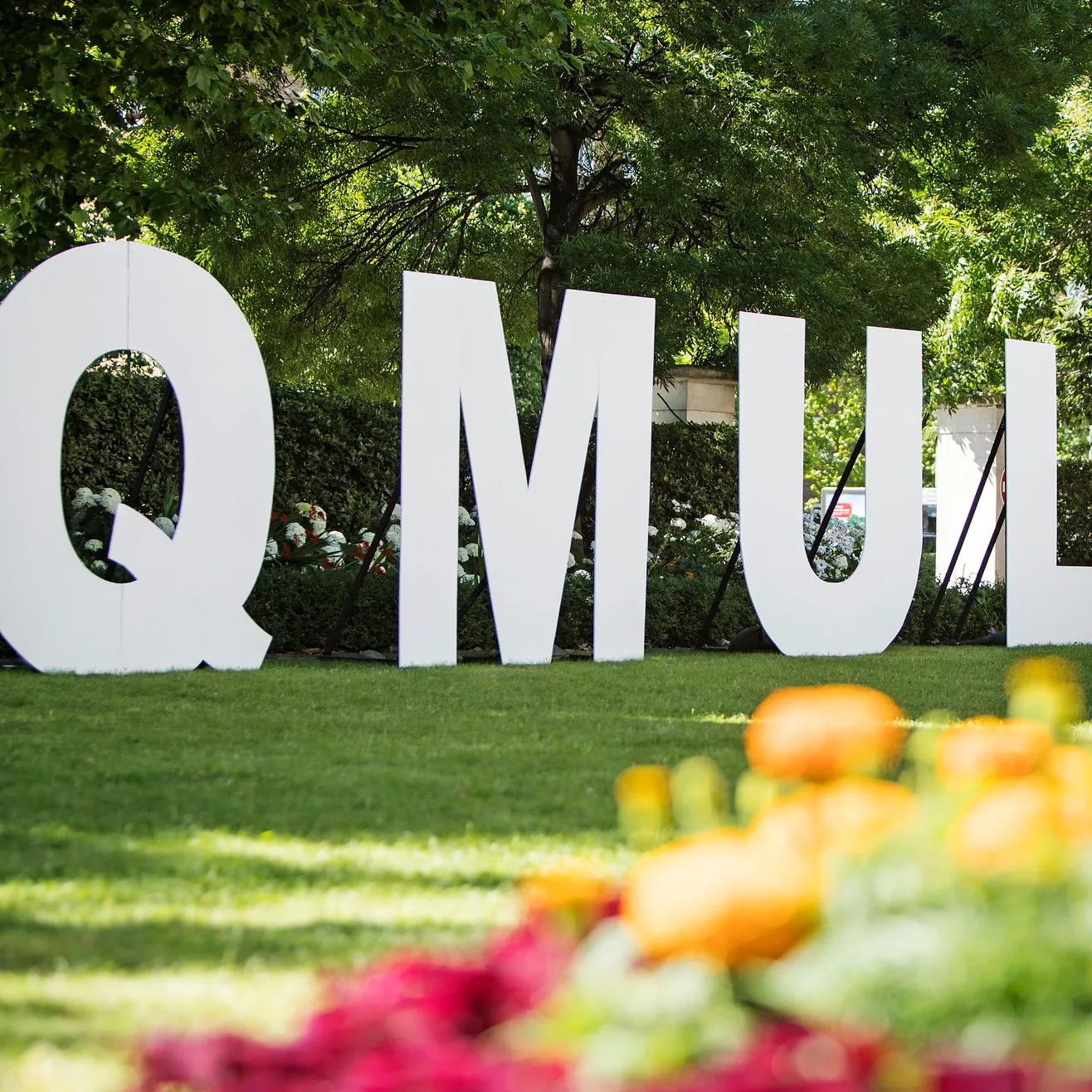 Large wooden letters on a lawn spelling out QMUL
