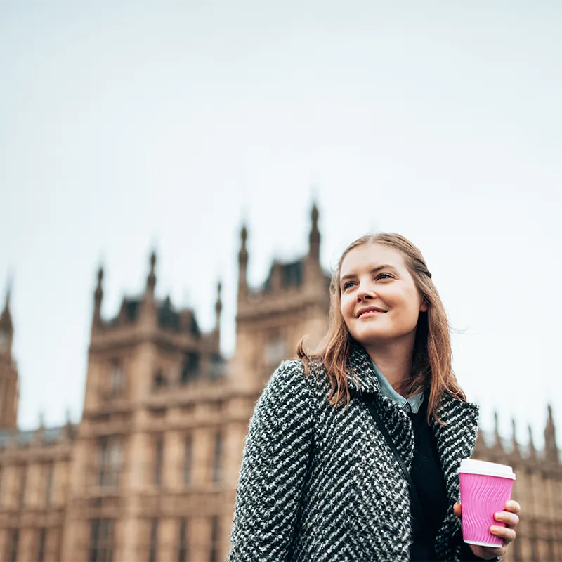 A girl with a pink coffee cup with Houses of Parliament in the background