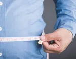 A man measures his waist with a measuring tape.