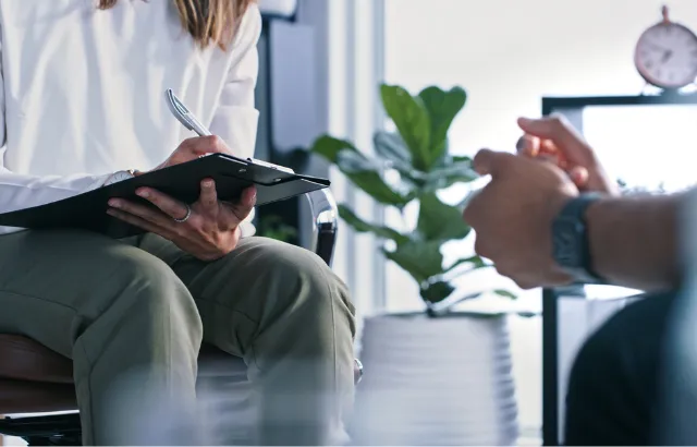 Female therapist writing notes while in session with a male patient.