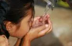 Young girl using her hands to drink water from a spout