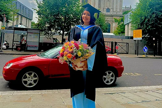 Student in graduation gown holding flowers looking at camera
