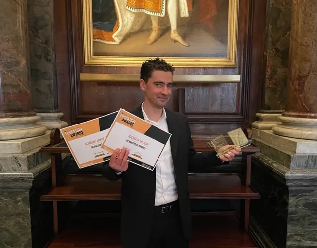 Tassos looking at camera holding awards