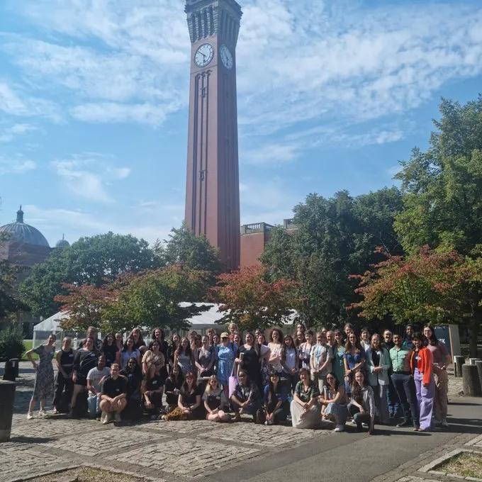 A group of students gathered in a green space in front of trees