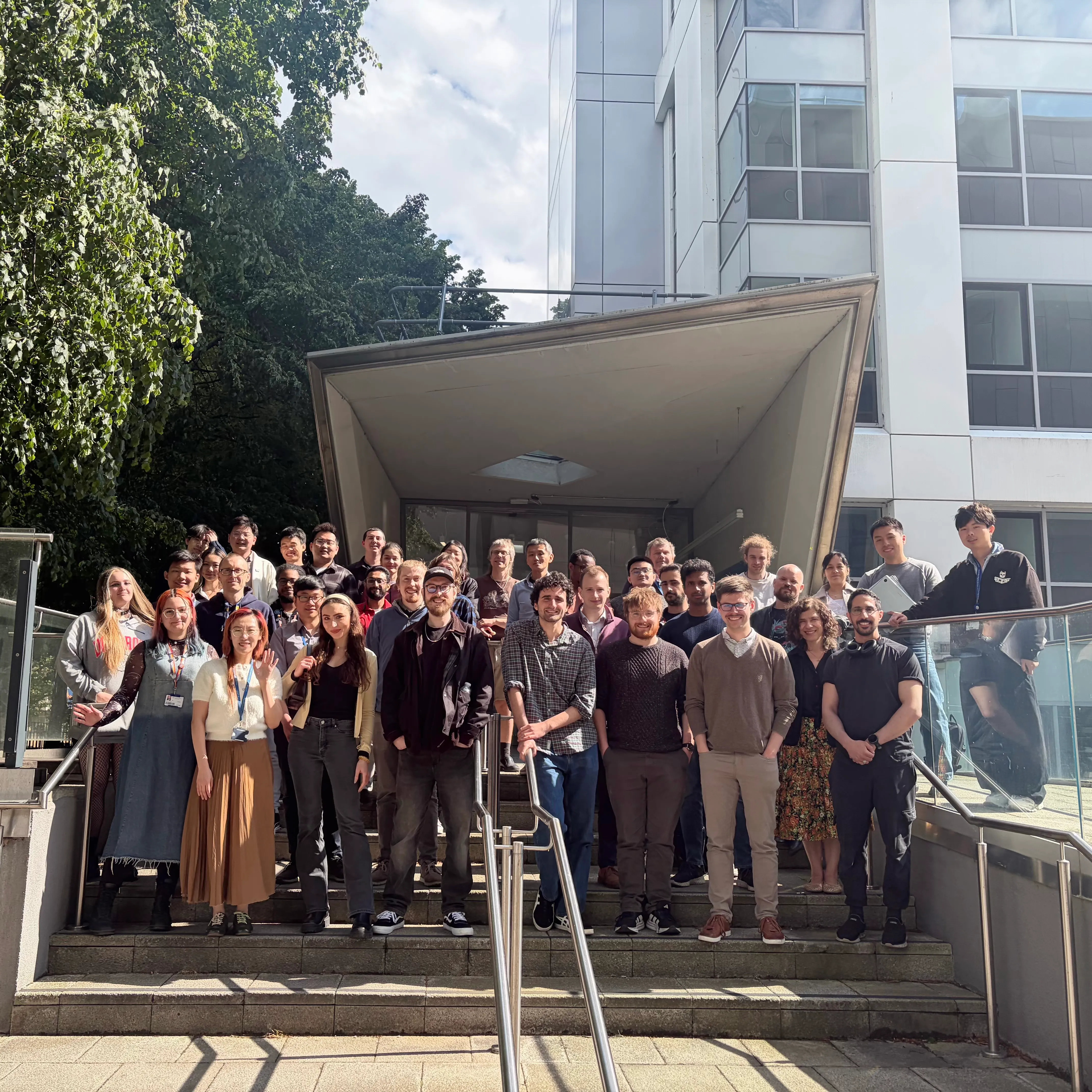 A group shot of people smiling, stood outside a building