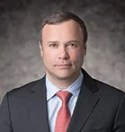 Dr Remy Gerbay in a grey suit, red tie and blue shirt against a grey bacground