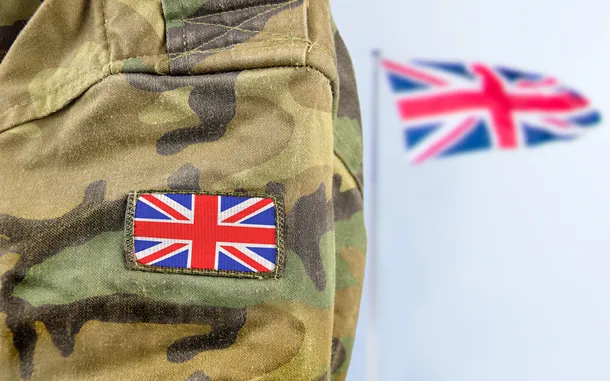 Close-up of army uniform with Union Jack patch, with Union Jack flag flying in background