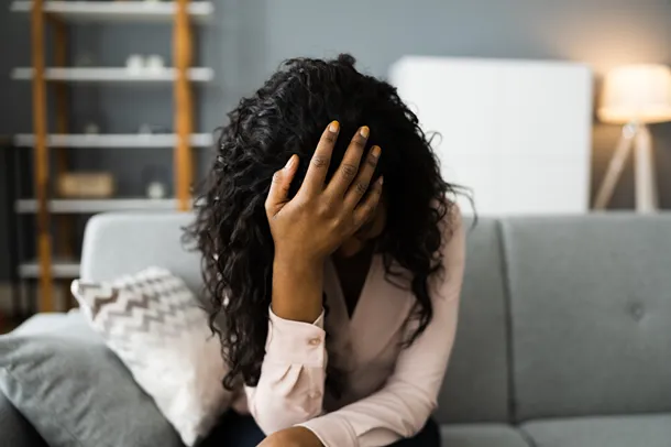 Person sits on a sofa with their head in their hands