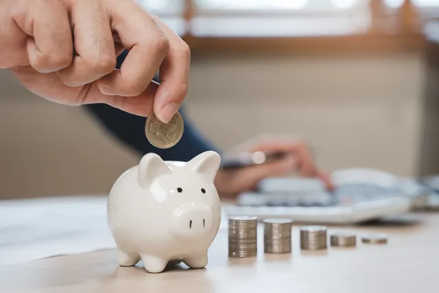 Piggy bank with coins near it; hand adding a coin to the piggy bank.