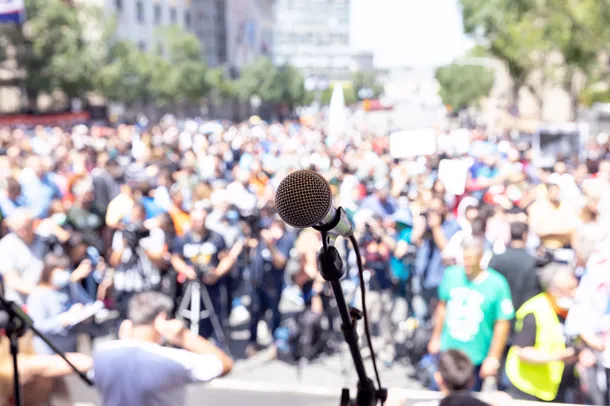 Crowd of people outside with a microphone on a stage in the foreground