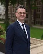 Professor Duncan Matthews in a suit and glasses standing in a garden