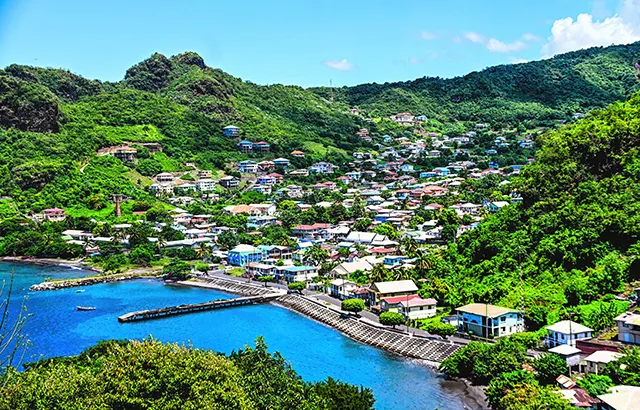 The port of Kingstown, Saint Vincent. There is a blue sea, and a port that leads to a town with budlings and trees.