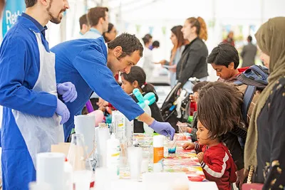 A Queen Mary staff member uses dye to colour water as children watch at the Festival of Communities