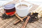 A cup of coffee and a cup of tea with tea leaves and coffee beans on a tablemat