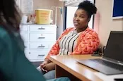 A woman is sitting at a desk speaking to her GP