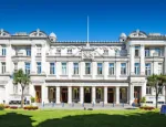 Picture of the neoclassical Queen's Building with a foreground of green grass and under a bright blue sky.