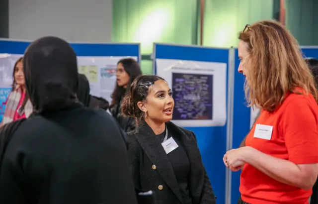 Two women speaking to each other in front of research poster boards