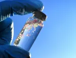 Gloved hand holding a small bottle containing microplastics
