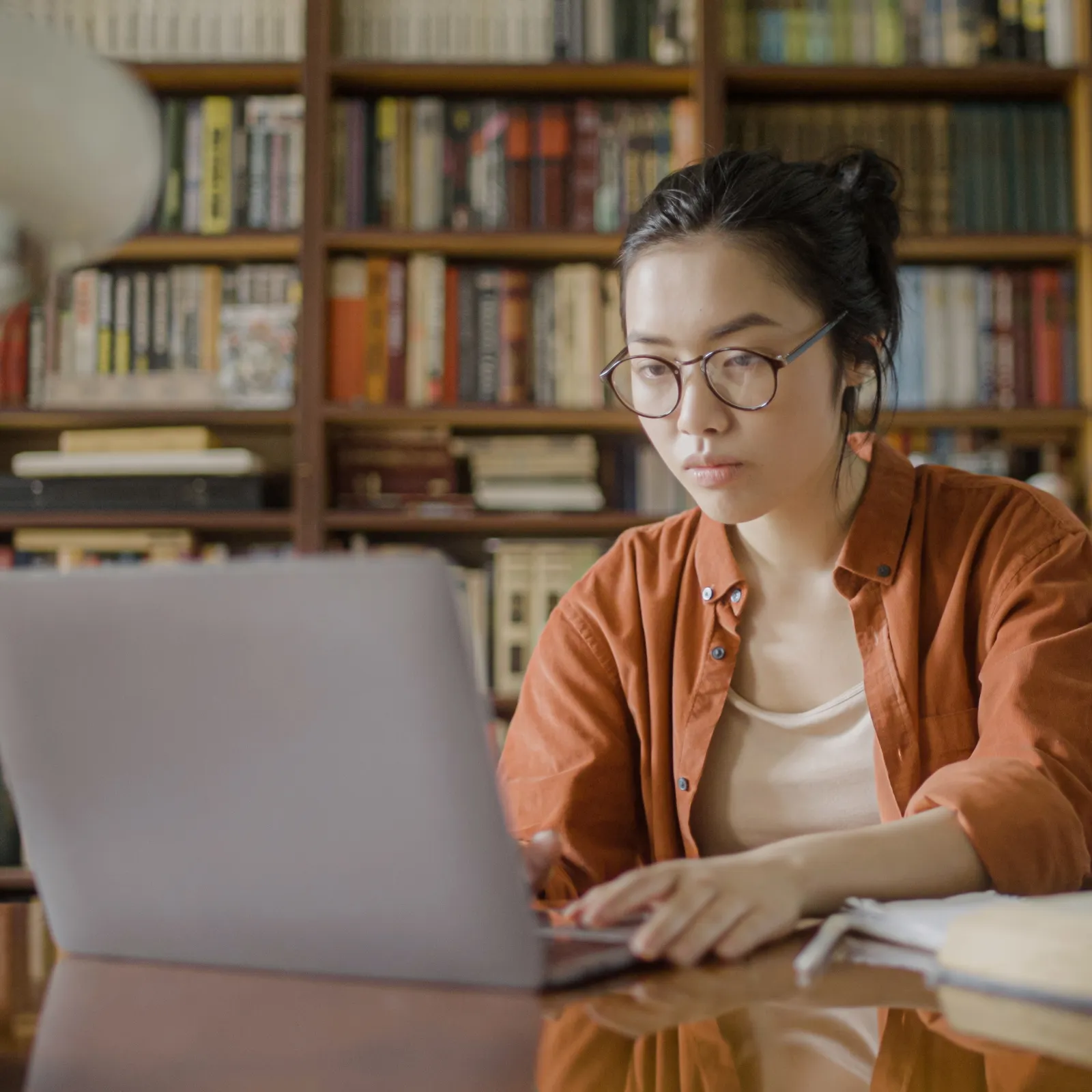 Girl wearing an orange sitting at a computer in a library
