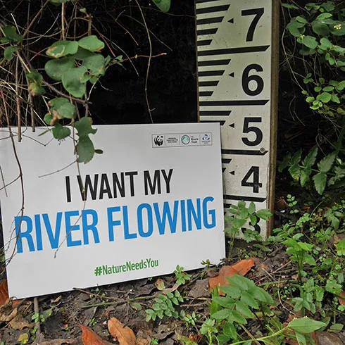 A dry riverbed with a river gauge board and sign stating 