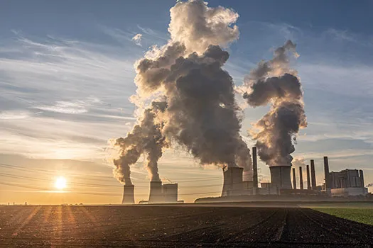 Smoke rising from cooling towers at a German coal-fired power station. It is dawn and the power station is by some fields.