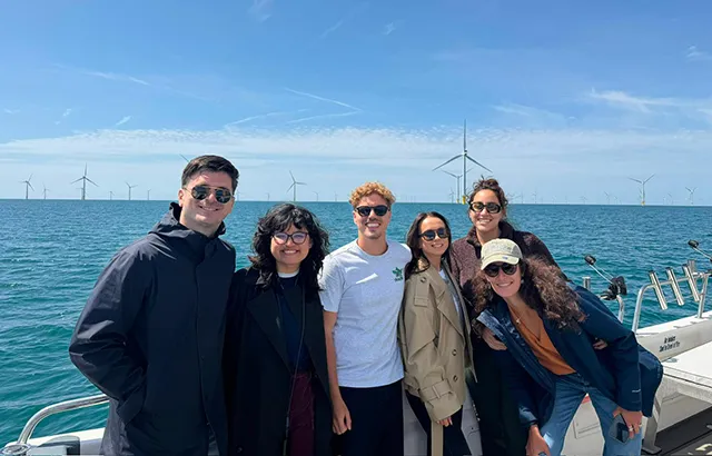 Queen MAry LLM students on a boat in the sea with a wind turbines behind them.
