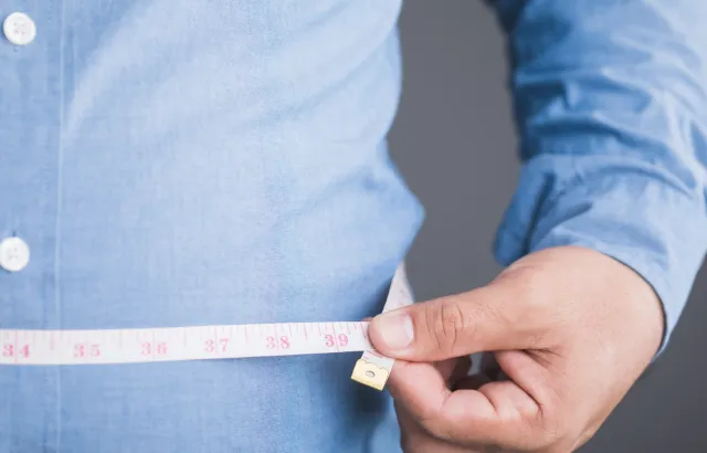 A man measures his waist with a measuring tape