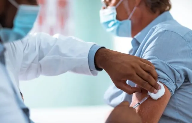 A man wearing a face mask is injected in his left arm with a hypodermic needle