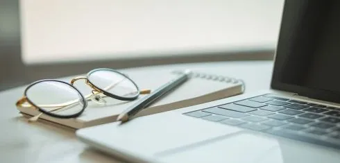 A laptop keyboard with a notebook and pen
