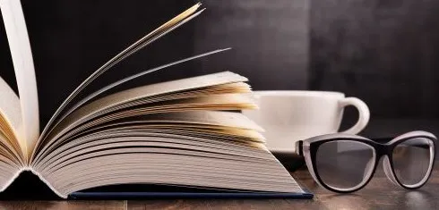 A cup of coffee next to an open book and a pair of glasses