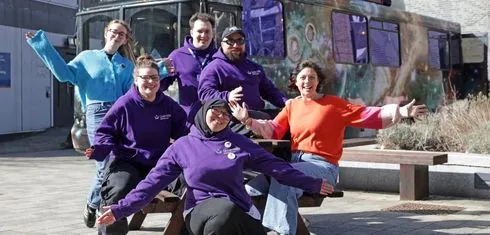 Student ambassadors, outreach officer, and artist sat on a bench next to moon palace bus