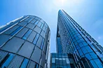 A view looking up from the ground at glass office buildings and a blue sky.