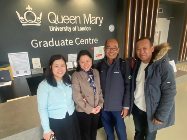 Four people smiling in the reception of the QMUL Graduate Centre.