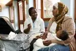 A woman sitting with her baby on her lap talks to a healthcare professional in a GP practice