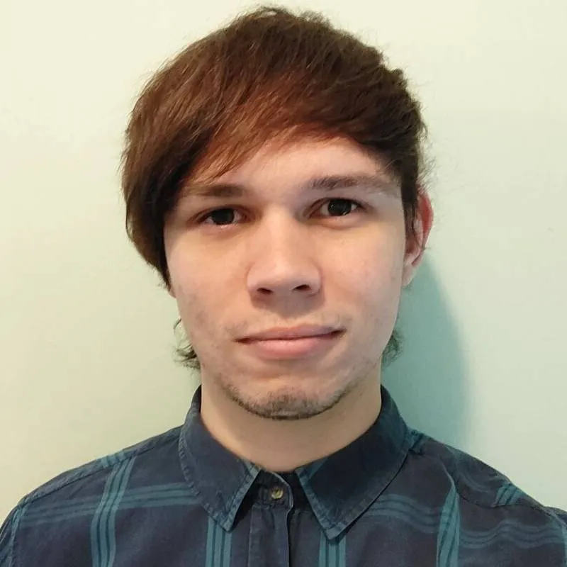 Bradley Desborough looking at the camera. Wearing a shirt and standing in front of a white background.