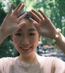 Photo of Xiaoyang Tong, student ambassador with their hands raised and smiling at camera