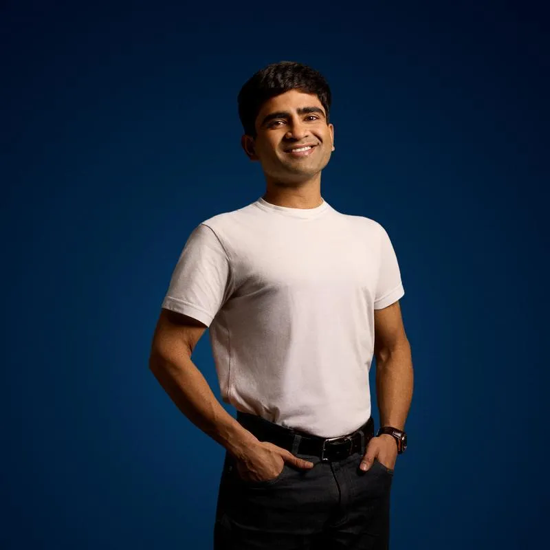 Student with white top and black jeans smiling, facing the camera against a blue backdrop