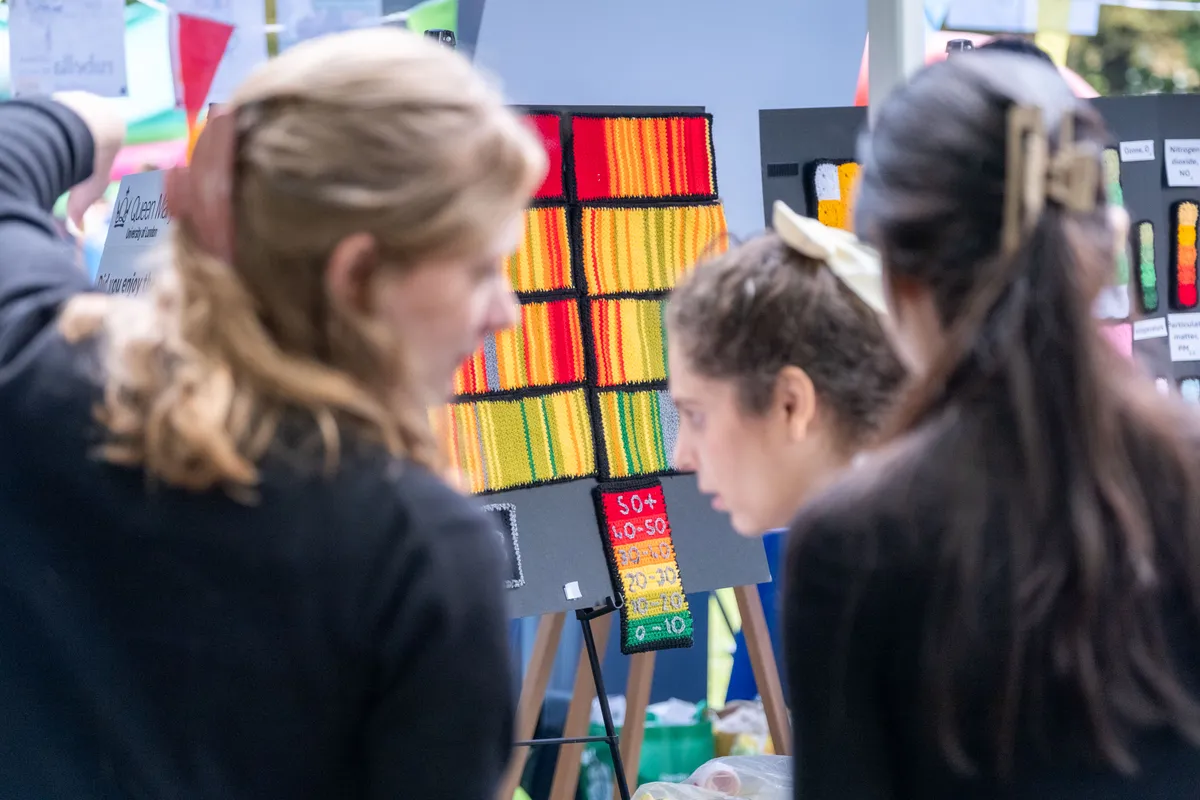 A close up of two people looking at a display of crocheted squares displaying air pollution data in different colours