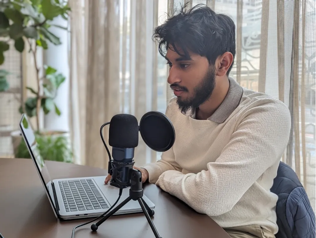 A boy sitting at a desk with a mic and laptop in front of him.