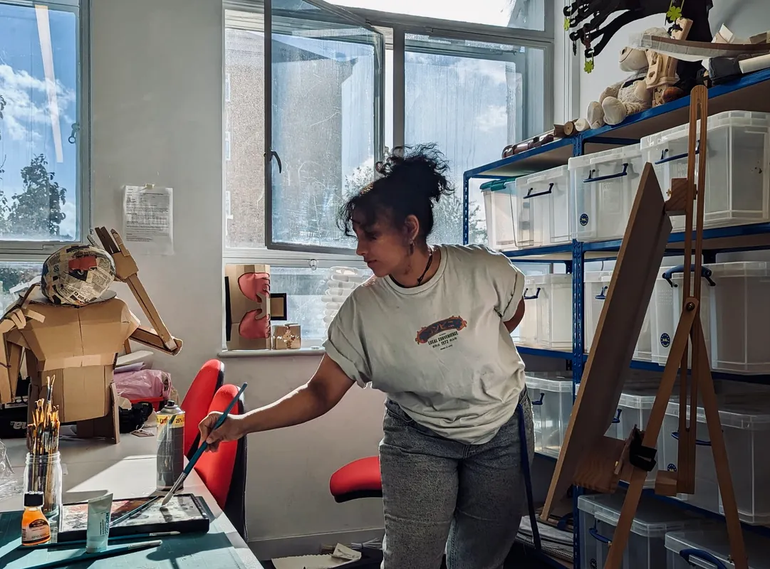 A girl painting with a desk to her left and her art piece to the right.