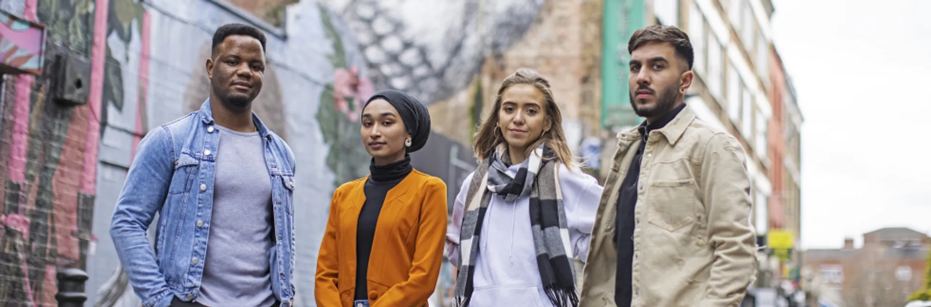 A group of four students standing in front of street art depicting a bird in London